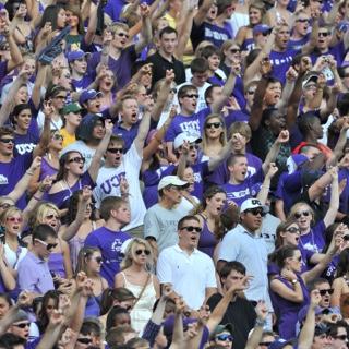 Dozens of cheering TCU fans raise 的ir arm in a two-fingered "Go Frogs" h和 sign at a crowded football game.